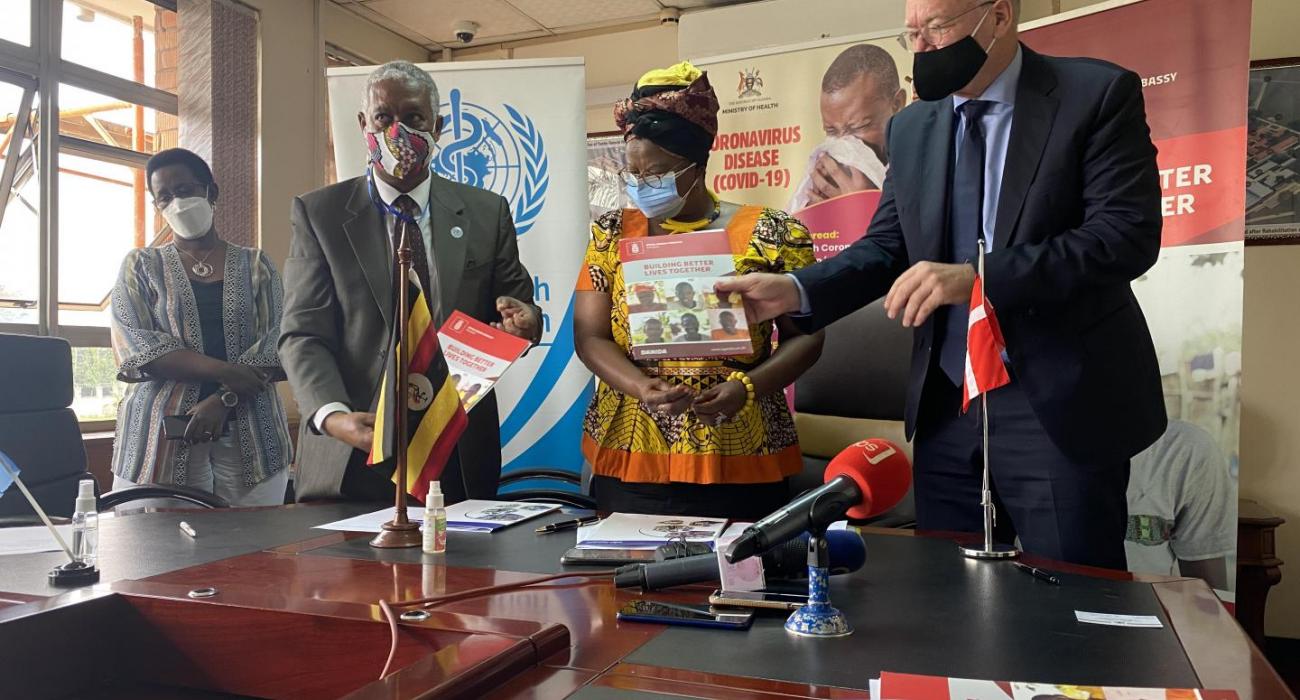 WHO Representative in Uganda, Dr Yonas Tegegn Woldemariam (white shirt) and Mr. Henrik Jespersen, the Head of Cooperation, Royal Danish Embassy in Kampala exchange signed agreements as Hon Hanifa Kawooya (yellow) and Dr Diana Atwine (white and black) look on at the Ministry of Health headquarters in Kampala