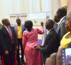 Minister of Health Dr Jane Ruth Aceng signs on a copy of the HSIRRP to launch the plan as government officials and partners look on 