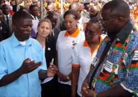 A Health Surveillance Assistant (in blue uniform) explains the procedure of preparing the Rotavirus vaccine to the Vice President as WR second from right looks on