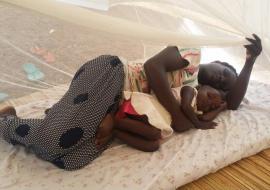 Mother and baby sleeping under a mosquito net  