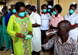 A TB patient receives treatment drugs from the Minister of Health on Sarah Opendi as other health workers look on 