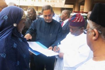 The Honourable Minister signing the hand-over documents while the WR watched